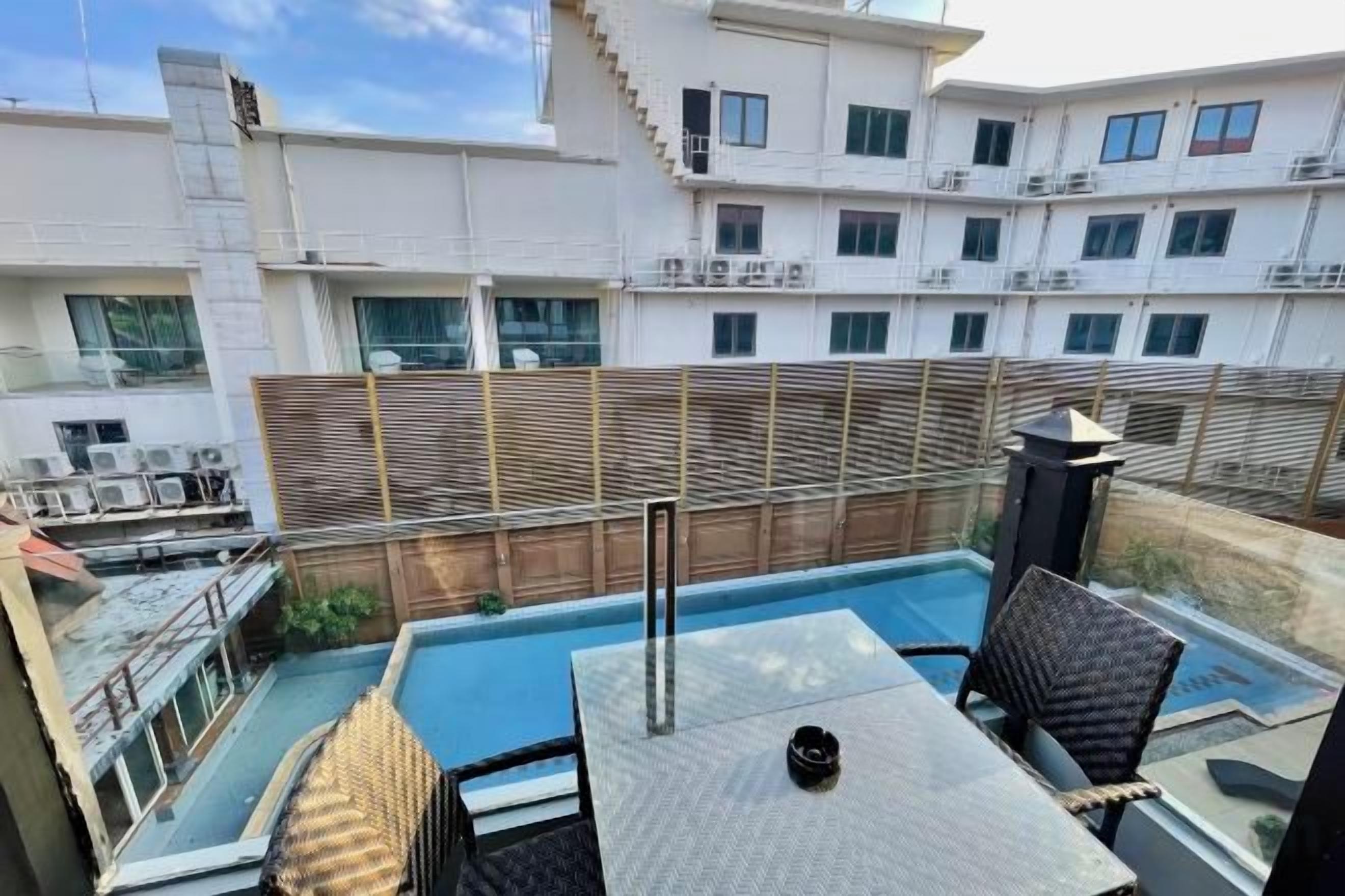 Un área de piscina en la azotea con una mesa y sillas, rodeada por una valla de madera y vistas a un edificio residencial.