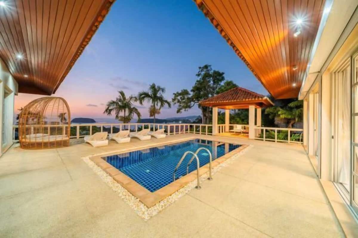A swimming pool with lounge chairs, a gazebo, and a view of palm trees and mountains.
