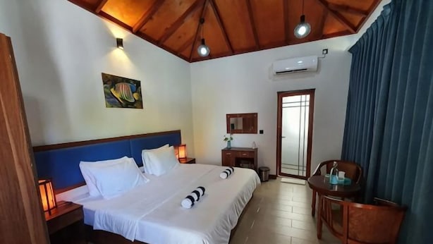 A hotel room with a bed, bedside lamps, a desk, a chair, a painting, and a door. - Blue Coral Vashafaru Maldives (Vashafaru)