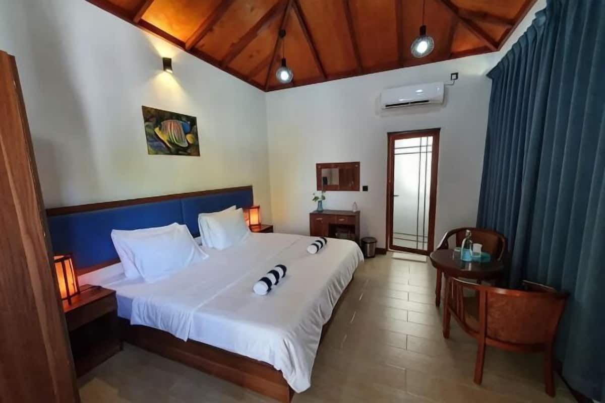 Ein Hotelzimmer mit Bett, Nachttischlampen, Schreibtisch, Stuhl, einem Bild und einer Tür.