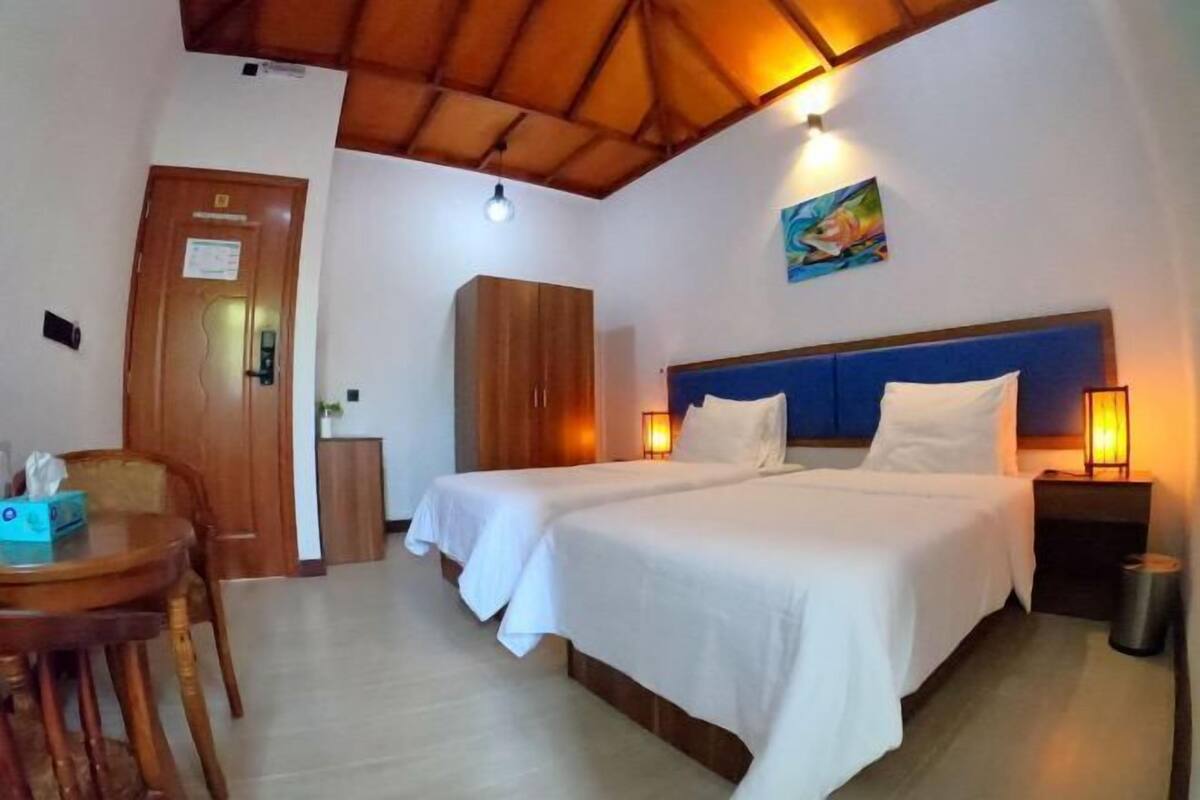 Ein Hotelzimmer mit zwei Betten, einem Holzschrank, einem Schreibtisch mit Stuhl und einem Bild an der Wand.
