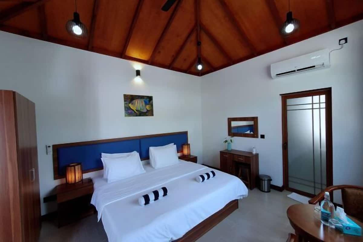 Ein Hotelzimmer mit Holzboden, einem Bett mit weißer Bettwäsche, einem Nachttisch mit Lampe, einem kleinen Tisch mit Stuhl und einer Badezimmertür.