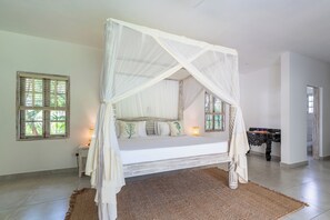 Quarto com cama de dossel, mesa de cabeceira, uma pequena mesa e vista para o exterior através de uma janela.