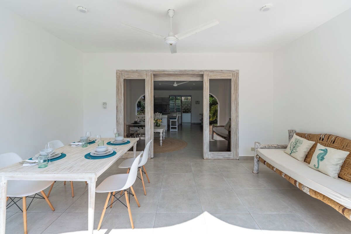 A modern dining area with a white table set for four, a wooden bench, and a ceiling fan.