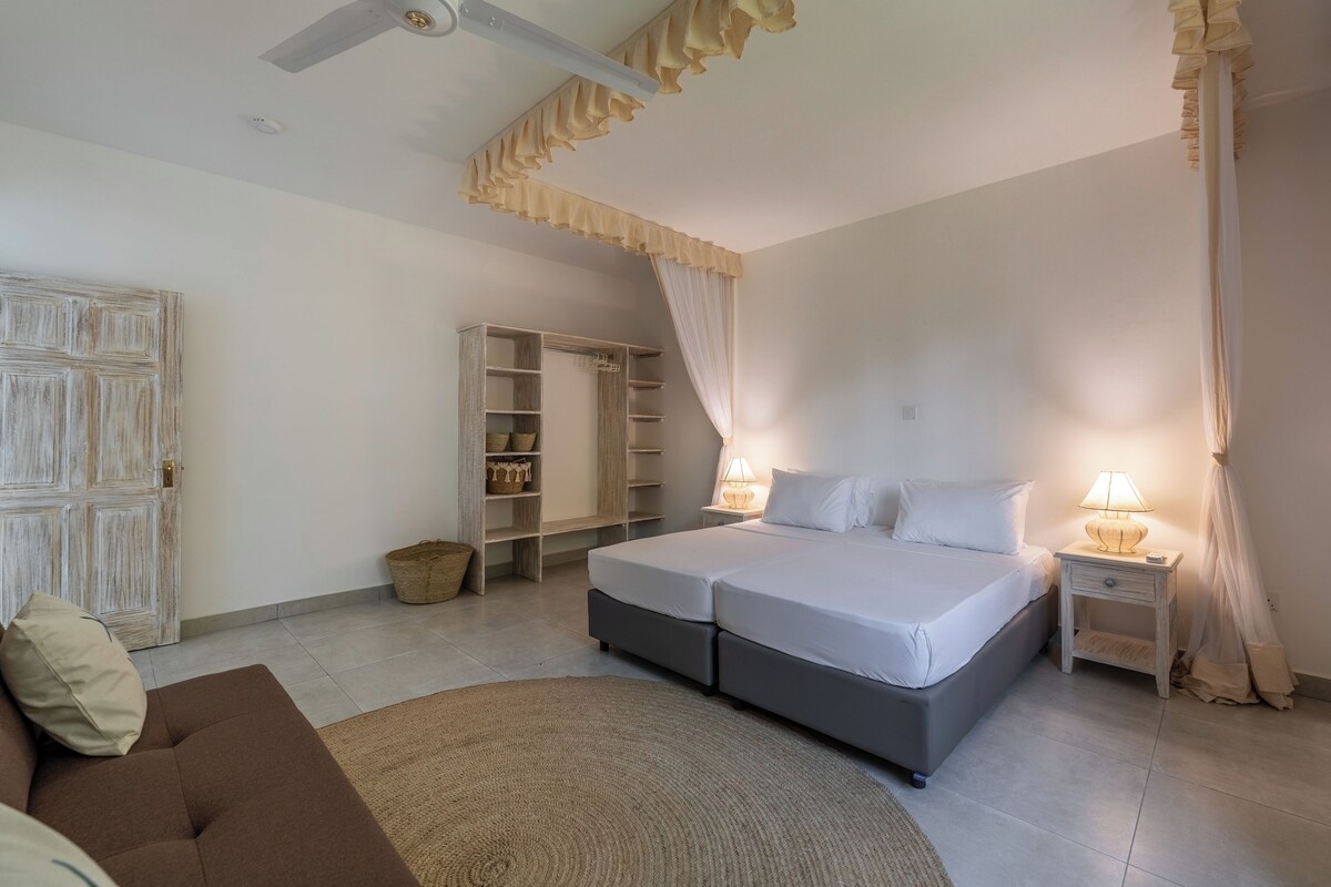 Quarto com cama, mesas de cabeceira, guarda-roupa e ventoinha no teto.