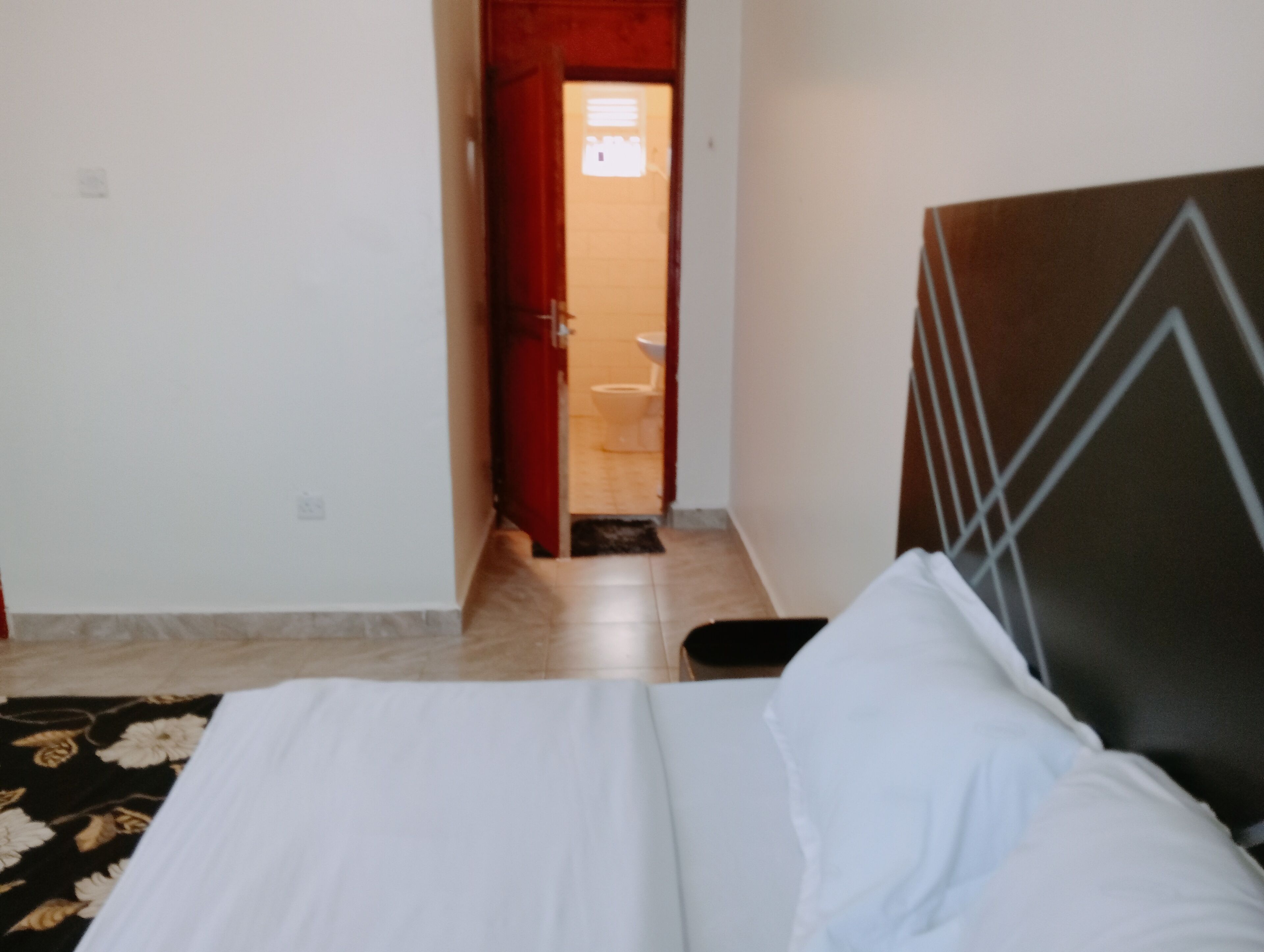 A hotel room with a bed, a red door, and a bathroom visible through the doorway.