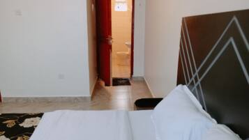 A hotel room with a bed, a red door, and a bathroom visible through the doorway.