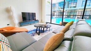A modern living room with a large sofa, a flat-screen TV, and a view of a swimming pool. - Pool Access Massive Townhouse (Bophut)