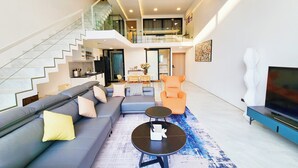 A modern living room with a grey sofa, a coffee table, and a TV. There is a staircase leading to an upper level. - Pool Access Massive Townhouse (Bophut)