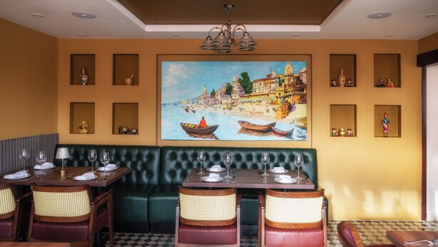 Un restaurant avec un sol à carreaux, des banquettes vertes rembourrées et une grande fresque représentant un paysage fluvial sur le mur.