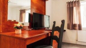 Un bureau en bois, une télévision, une chaise et un vase de fleurs.