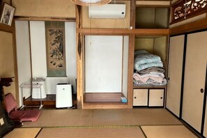 Una habitación tradicional japonesa con suelo de tatami, un futón, un pequeño calentador, un lavabo y una puerta corredera.
