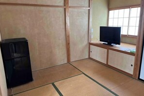 Een kamer met tatami vloerbedekking, een televisietoestel op een lage standaard en een kleine, zwarte koelkast.