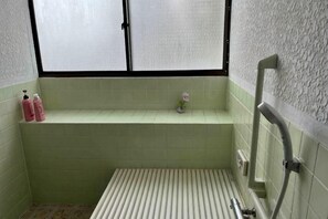 Un baño con ventana, repisa con artículos de aseo y zona de ducha.