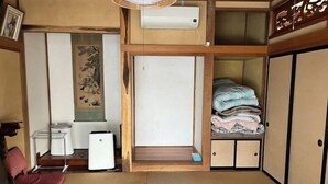 Une pièce de style japonais traditionnel, avec un sol recouvert de tatamis, un paravent en papier de riz (shoji), un futon, un petit radiateur et une étagère où sont pliés des vêtements.