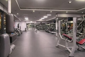 A gym with treadmills, weight machines, and a mirrored wall. - Cosmos Living Cozy Studio With Balcony (Dubai)