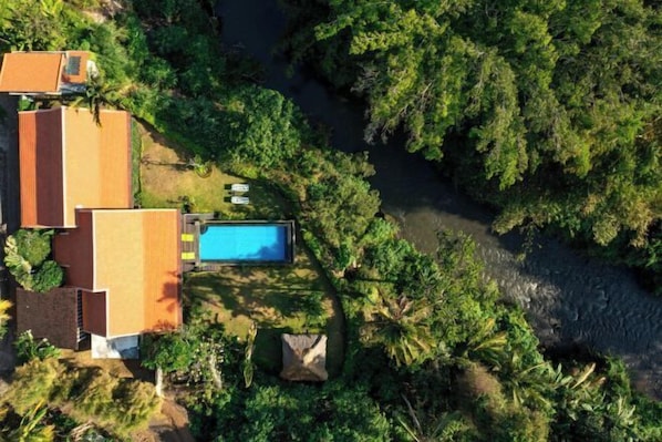 An aerial view of a property with a swimming pool, surrounded by lush greenery and a river. - Villa Lepak by the River (Bali)