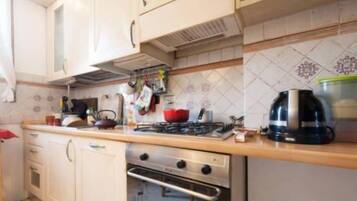 Una cocina con armarios blancos, estufa, horno y hervidor.