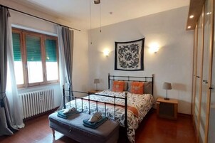 Un dormitorio con cama, mesitas de noche, un radiador y una ventana con cortinas.