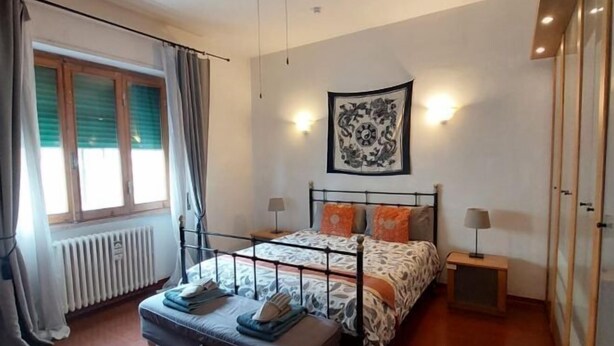 Une chambre à coucher avec un lit, des tables de chevet, un radiateur et une fenêtre avec des rideaux.