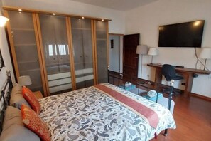 Un dormitorio con cama, escritorio, silla, televisor y armario.