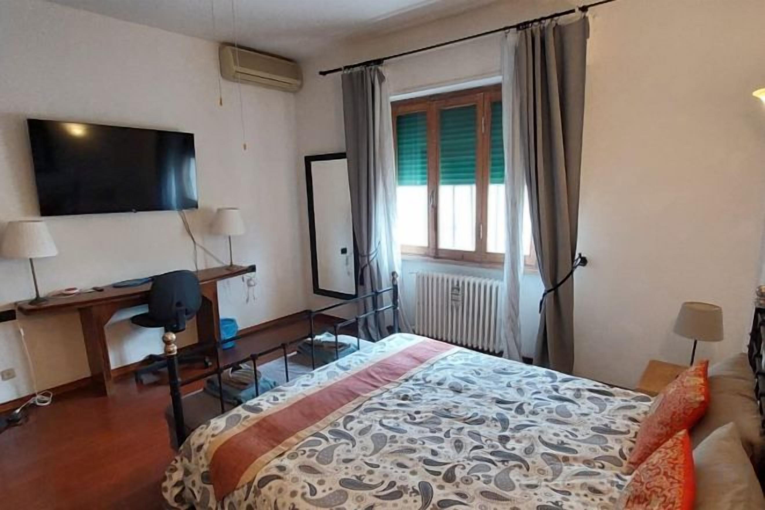 Une chambre d’hôtel équipée d’un lit, d’un bureau, d’une chaise, d’une télévision et d’une fenêtre avec des rideaux.