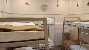 Une chambre de dortoir avec des lits superposés, un ventilateur et des décorations murales.