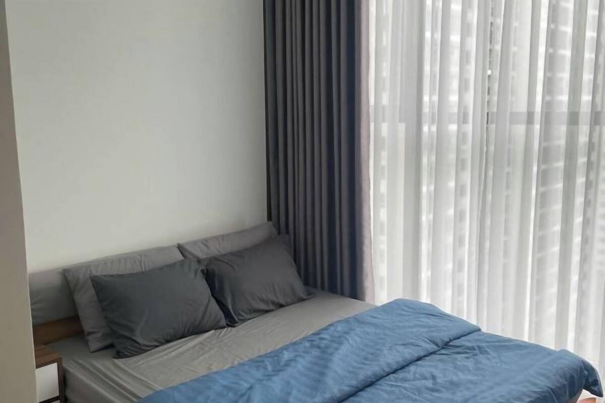 Una cama con ropa de cama gris, una manta azul y almohadas grises.