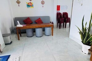A reception area with a wooden bench, red chairs, a potted plant, and a white trash bin. - Sea Home Homestay (Phan Thiet)