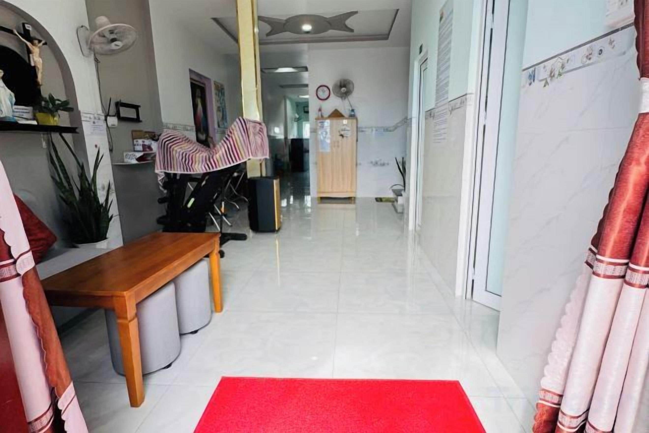 A hotel lobby with a red carpet, a wooden bench, a fan, and a view into the corridor.