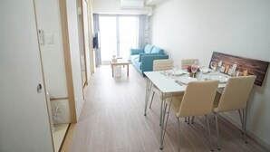 A dining area with a table set for four, a sofa in the background, and a door leading to another room. - Shinsaibashi H2H 901 (Osaka)