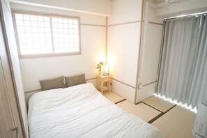 Un dormitorio con una cama, una mesita de noche con lámpara, una ventana con vistas y una cortina.