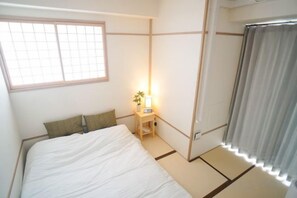 Una habitación con una cama, una mesita de noche con lámpara, una ventana y una puerta corredera.