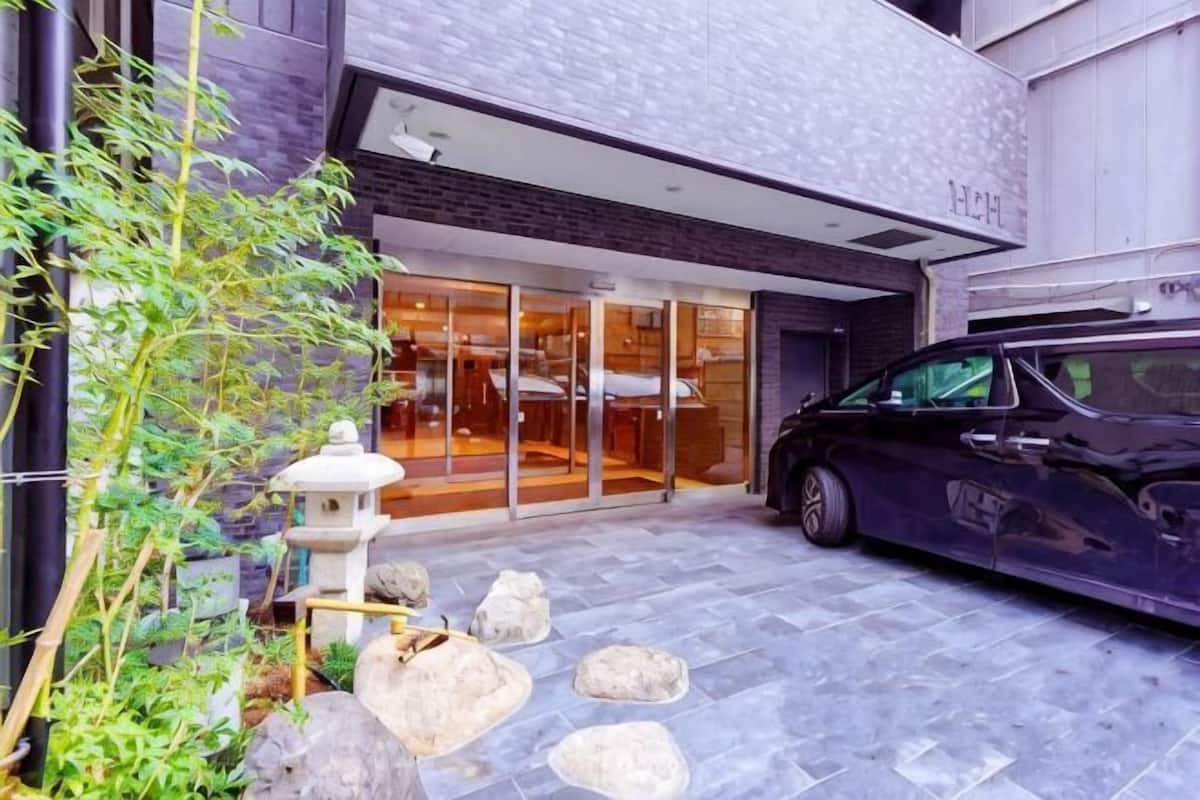 A modern building with a car parked in front, a stone pathway, and a small garden area with a stone lantern.