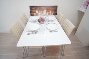 A dining table set for four with candles, a vase of flowers, and a wooden headboard.