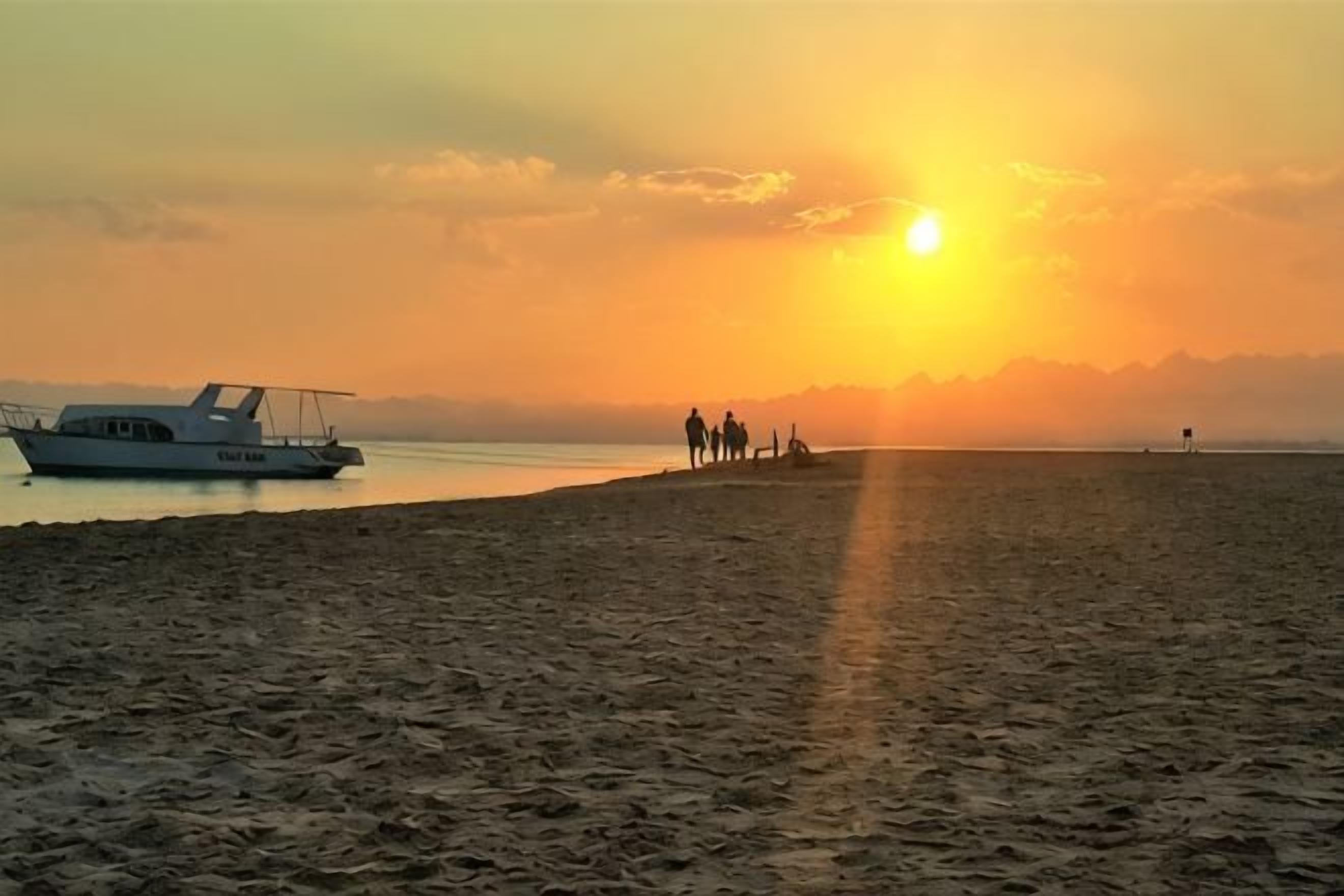 Uma praia com um barco e pessoas caminhando pela orla durante o pôr do sol.