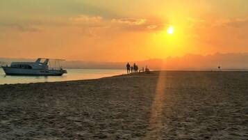 Uma praia com um barco e pessoas caminhando pela orla durante o pôr do sol.