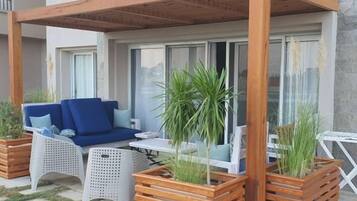 Un espacio de estar al aire libre con una pérgola de madera, muebles de mimbre blanco y plantas en macetas.