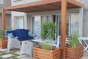 An outdoor seating area with a wooden pergola, white wicker furniture, and potted plants. - Luxury Apt - Soma Bay - Hurghada -Next to Breakers (Qesm Safaga)