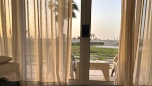 A room with a large sliding glass door leading to an outdoor area with a view of a green landscape and palm trees.