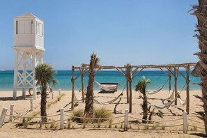 Una playa con una torre blanca, una hamaca y un bote.