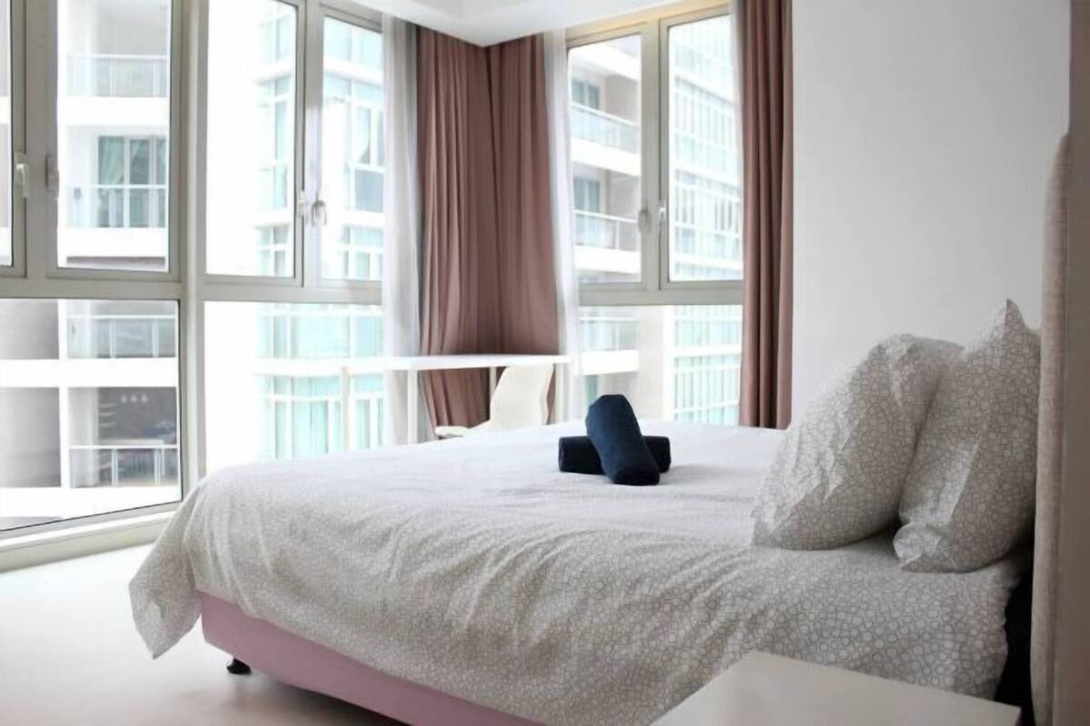 A hotel room with a large bed, a desk, and a view of buildings through large windows.