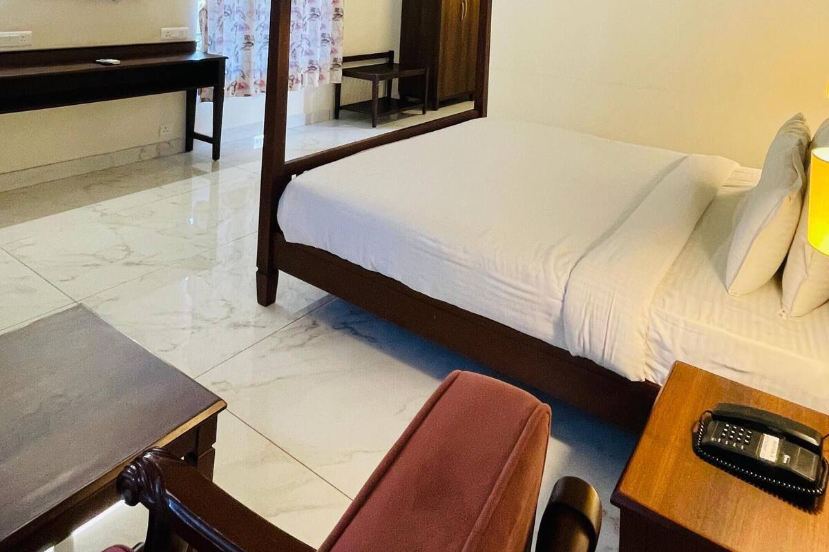 Een hotelkamer met een bed, een bureau, een stoel, een televisie en een plafondventilator.