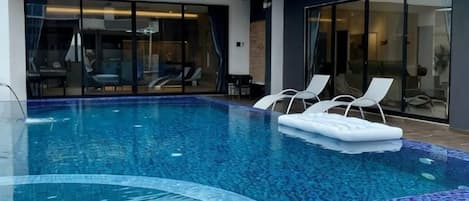 A swimming pool with lounge chairs and a glass door leading to a room.