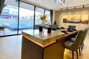 A modern kitchen with a marble countertop, dining area with chairs, and a large window overlooking a swimming pool. - Oasis Villa Homestay Kuala Selangor (Kuala Selangor)