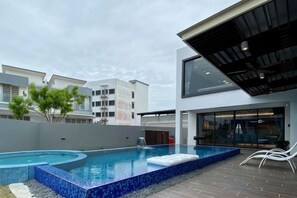 A modern outdoor swimming pool with a curved design, surrounded by a low wall and a paved deck. - Oasis Villa Homestay Kuala Selangor (Kuala Selangor)