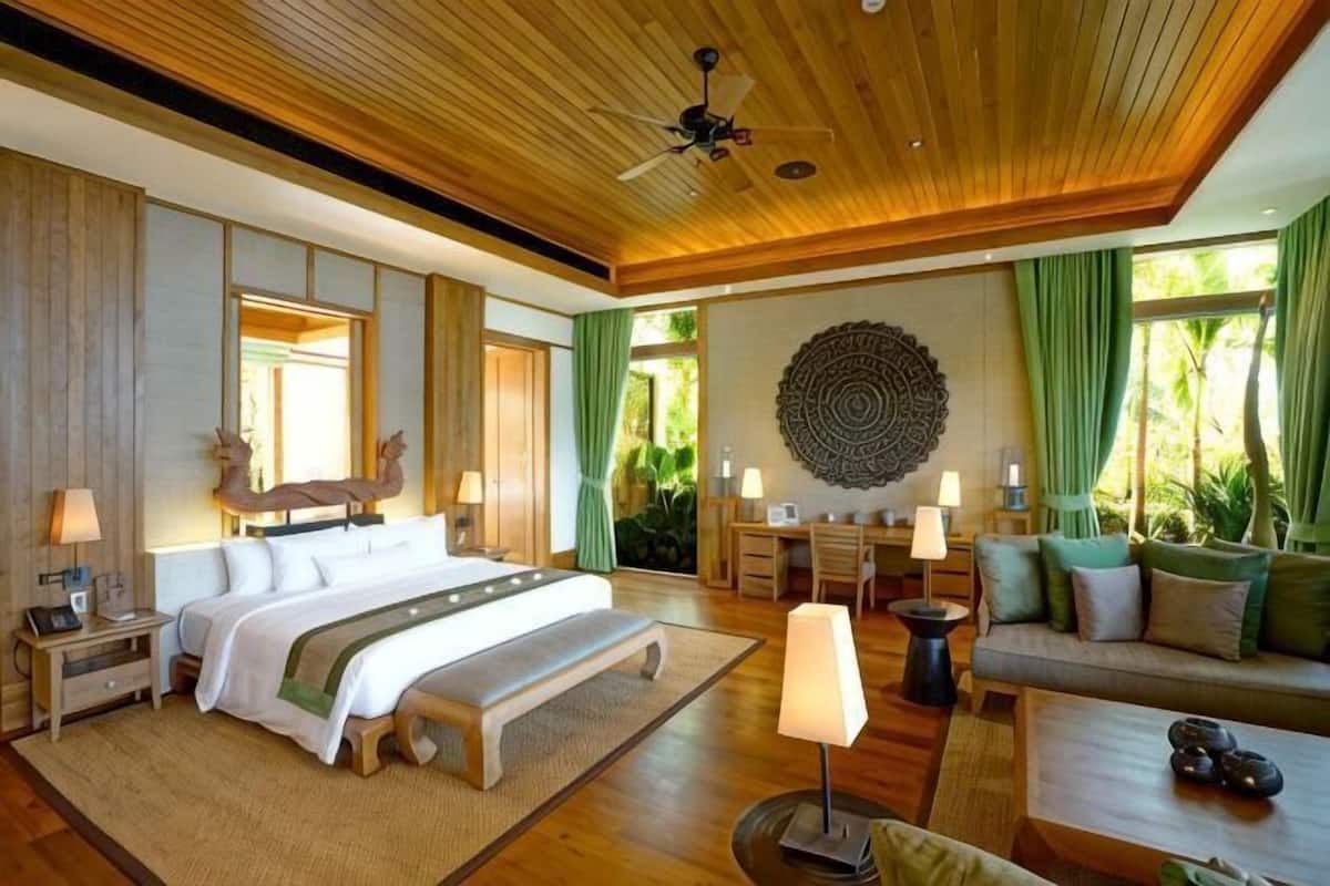 A spacious bedroom with a large bed, bedside tables, a bench, and a seating area with a sofa and armchairs.