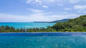 An infinity pool with clear blue water, surrounded by lush greenery and overlooking a turquoise sea and distant mountains. - The Sawan (Phuket)
