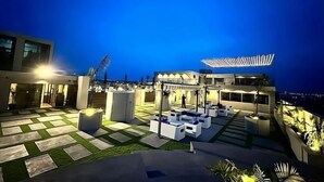 A rooftop terrace with outdoor seating, a pergola, and a view of the city at night. - The Skyluxe (Islamabad)