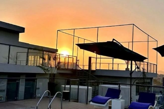 A modern building with a glass facade, a pool area with lounge chairs, and a staircase leading to an upper level.